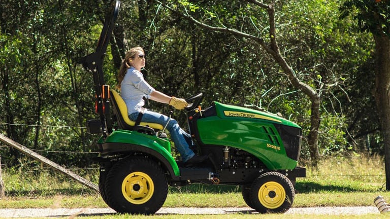 Femme conduisant un tracteur compact 1023E sur un chemin de terre