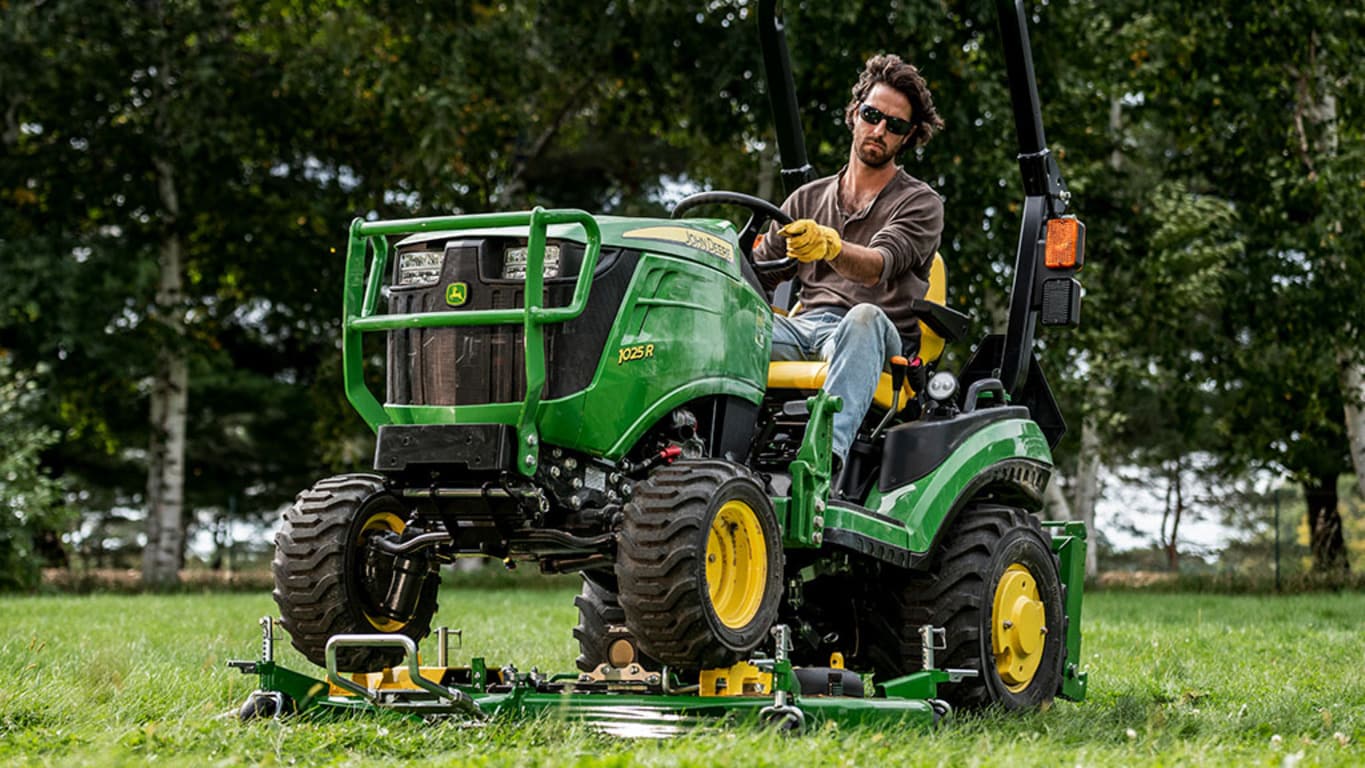 A yard being mowed by a green compact tractor on an AutoConnect mid-mount mowing deck.