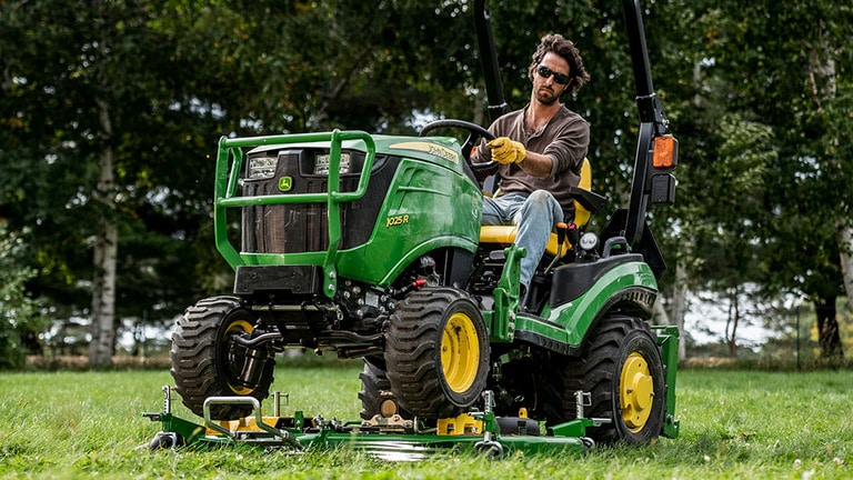 A yard being mowed by a green compact tractor on an AutoConnect mid-mount mowing deck.