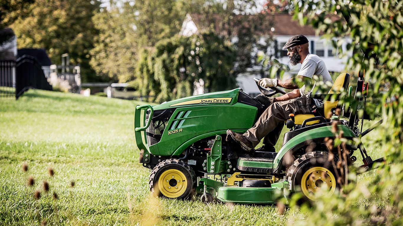 person riding green and yellow compact tractor 1025r