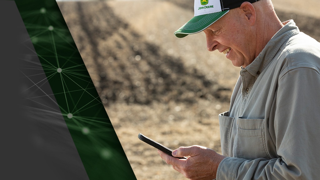 Photo of farmer monitoring a John Deere Autonomous 8R Tractor on his smartphone.
