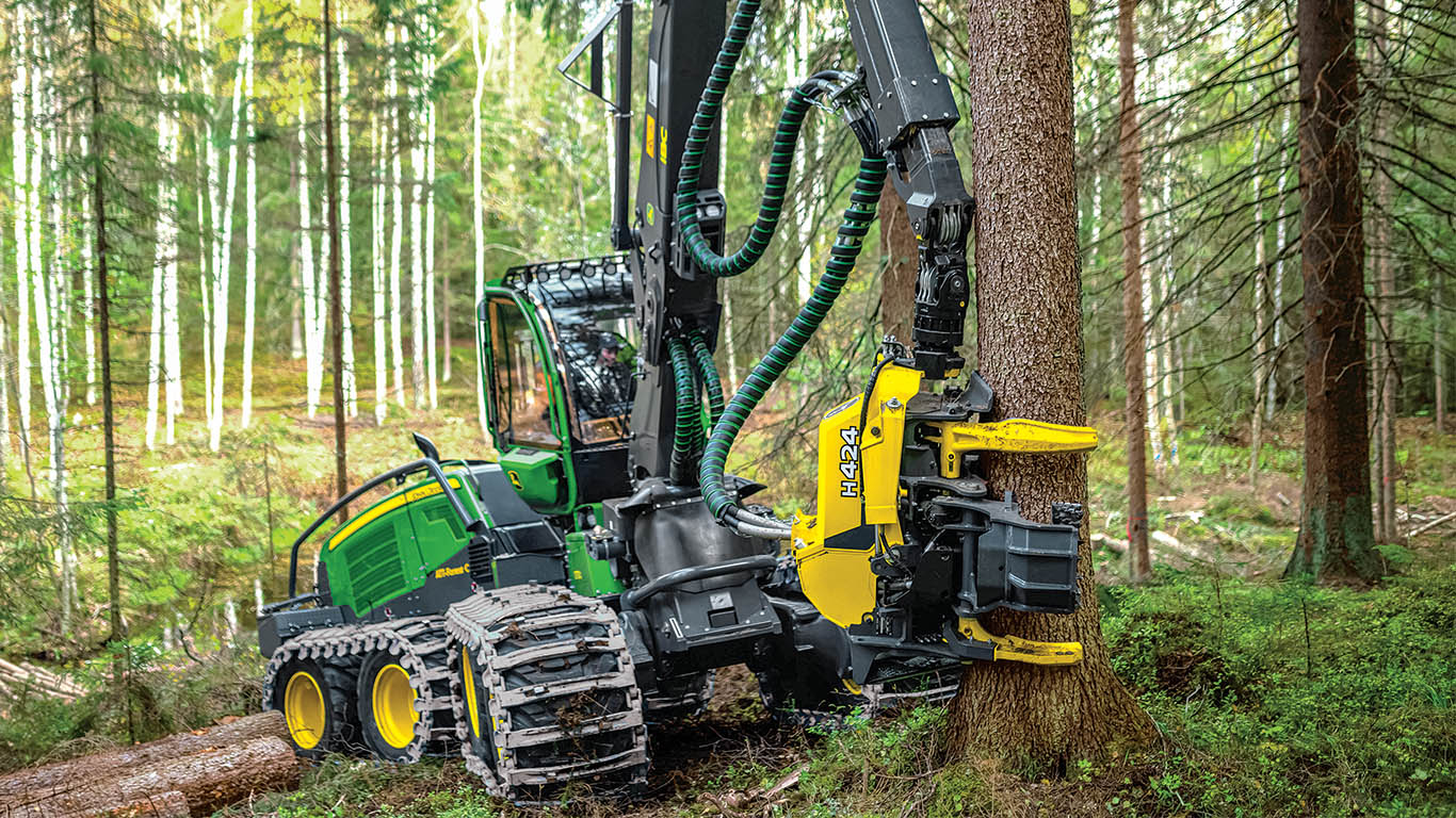 Une abatteuse-façonneuse à roues John&nbsp;Deere qui abat un arbre dans une forêt enneigée.