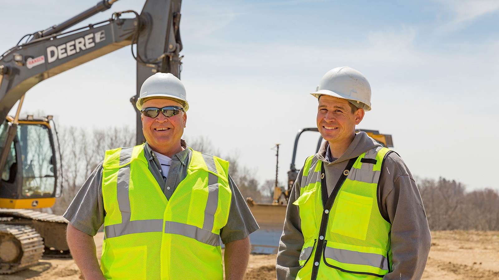 Rich and Matt Gansen stand in front of their John Deere Excavator