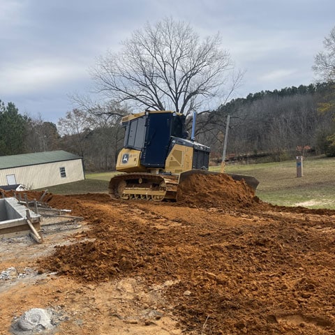 A John Deere 450 P-Tier dozer grading dirt next to a concrete form.
