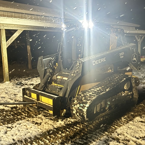 Chargeuse 333 de catégorie P avec une pointe à balles en train de chauffer tandis que la neige tombe autour d'elle.