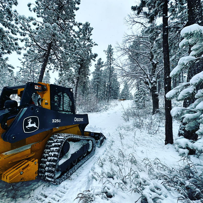 Chargeuse à direction différentielle 325G John Deere avançant dans la neige.