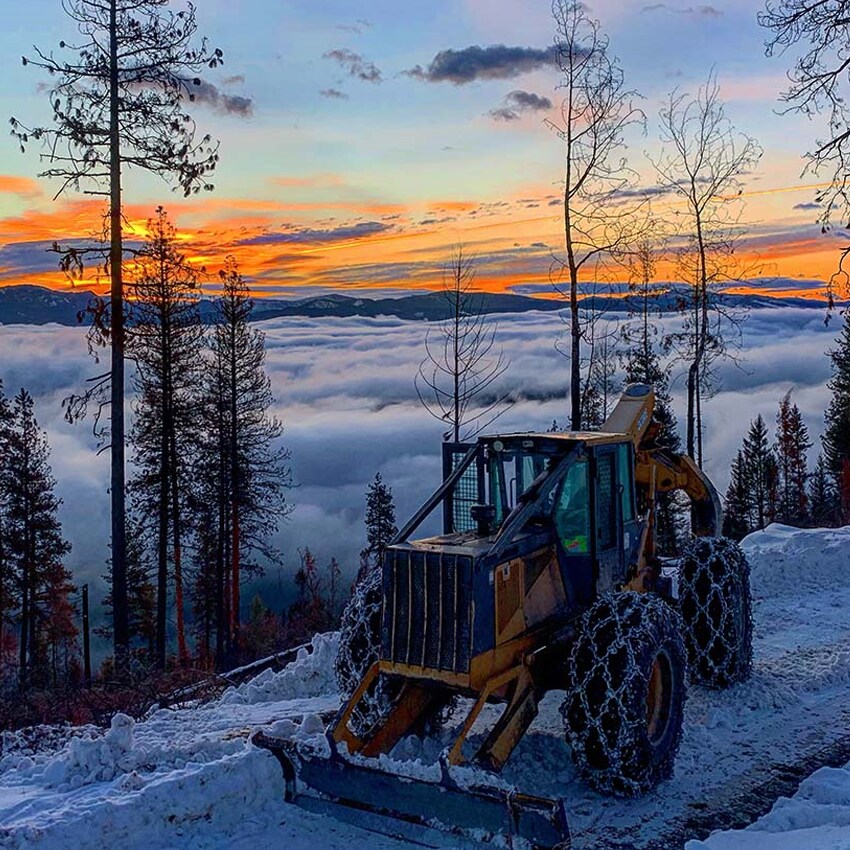 Tracteur avec chargeuse de John Deere poussant de la neige sur un chemin de terre sinueux.