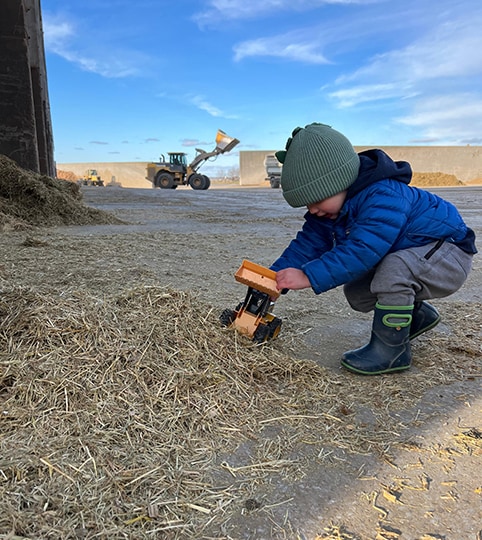 Child playing with a toy replica of a John&nbsp;Deere wheel loader, with the real-life version at work in the background.