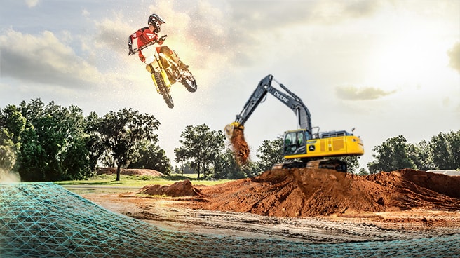 Un pilote de motocross saute dans les airs pendant que l’excavatrice SmartGrade™ 350G LC de John &nbsp;Deere façonne l’un des sauts sur le parcours.