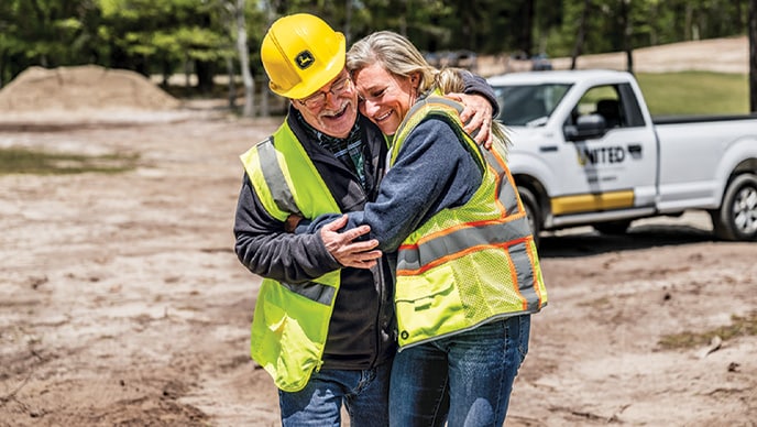 Jennifer Morris, de GFM Enterprises, et Joe Huber, de United Construction & Forestry, rient et se serrent dans leurs bras dans un chantier à Cape Cod. 