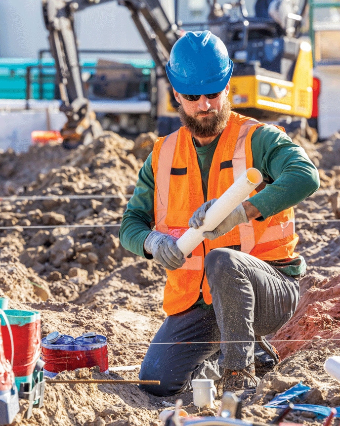 Un travailleur ajuste des conduites souterraines sur un chantier