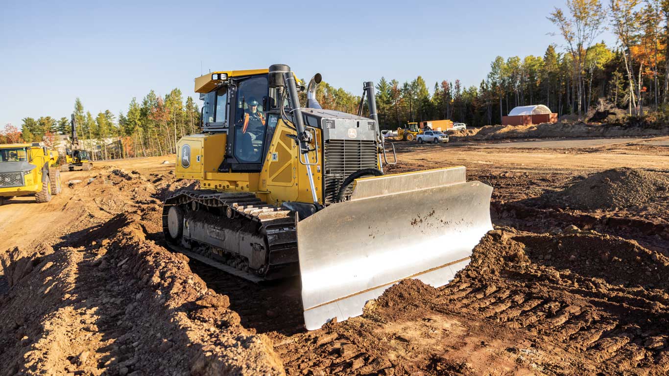 Tracked bulldozer pushing soil at an active construction site with trees and equipment in the background