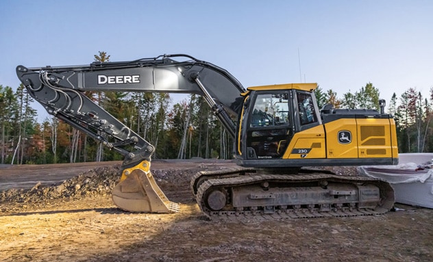 John&nbsp;Deere tracked excavator parked at a construction site with barriers and trees in the background.