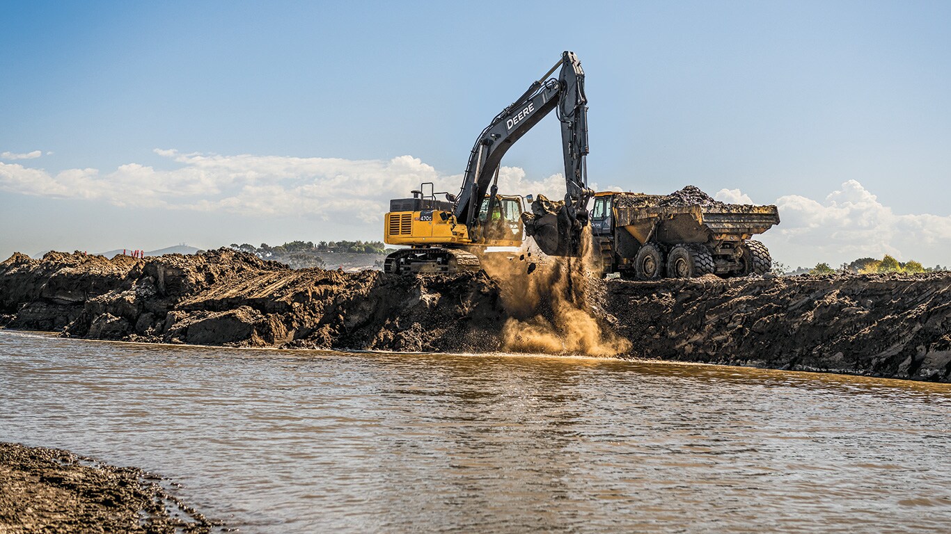 Une excavatrice 470G LC de John Deere déplace un godet rempli de terre d’une lagune pour le déverser dans un camion articulé à benne basculante 410E-II.