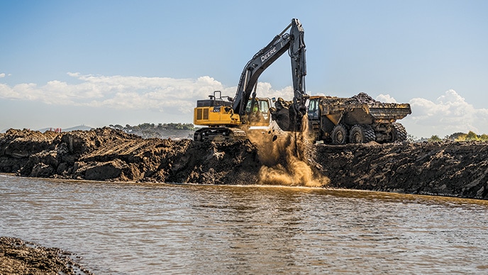 Une excavatrice 470G LC de John Deere déplace un godet rempli de terre d’une lagune pour le déverser dans un camion articulé à benne basculante 410E-II.