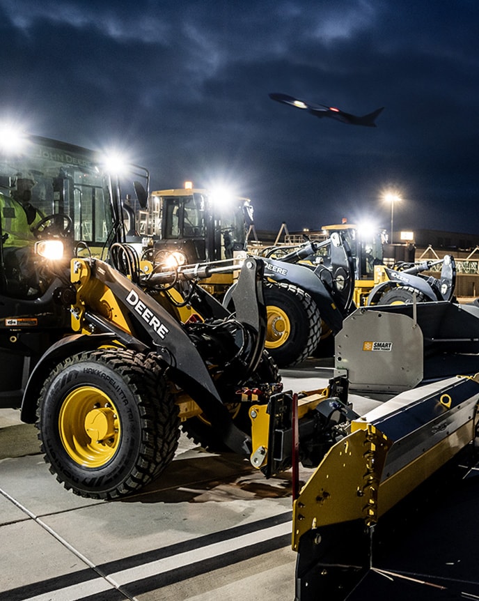 As the sun rises on a cold December morning, Aaron Kaden, Fleet Asset Superintendent, walks past John Deere 644 X‑Tier Wheel Loaders, 844L Wheel Loaders, and 244L Compact Wheel Loaders near the new terminal at Kansas City International Airport.