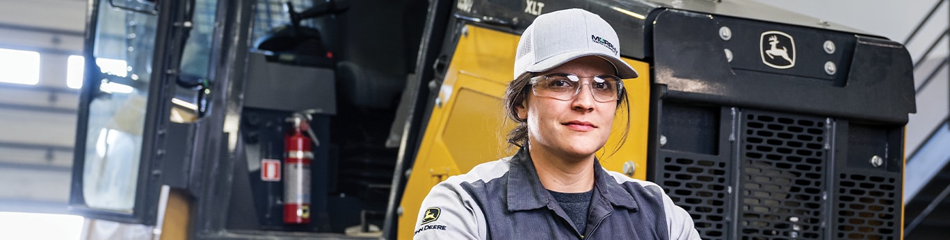 Photo de Sarah Davidson devant un bouteur de John Deere dans un atelier