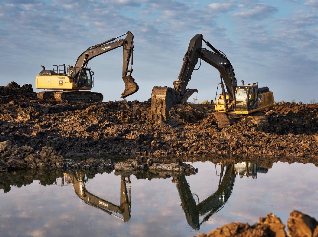 A 350G LC and a 210G LC SmartGrade Excavator use their buckets to empty a pond of its water.