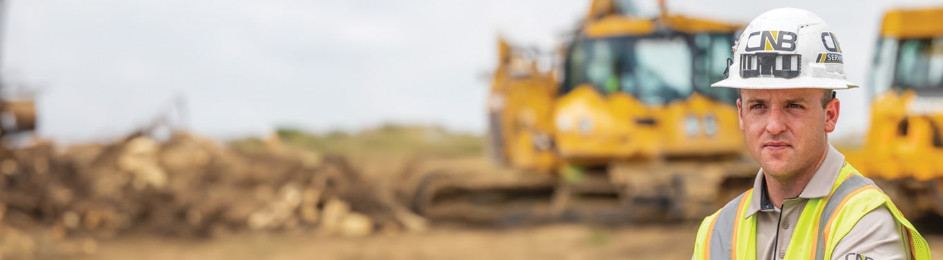 Travailleur en tenue de sécurité sur un chantier de construction en terre avec des bouteurs jaunes en arrière-plan