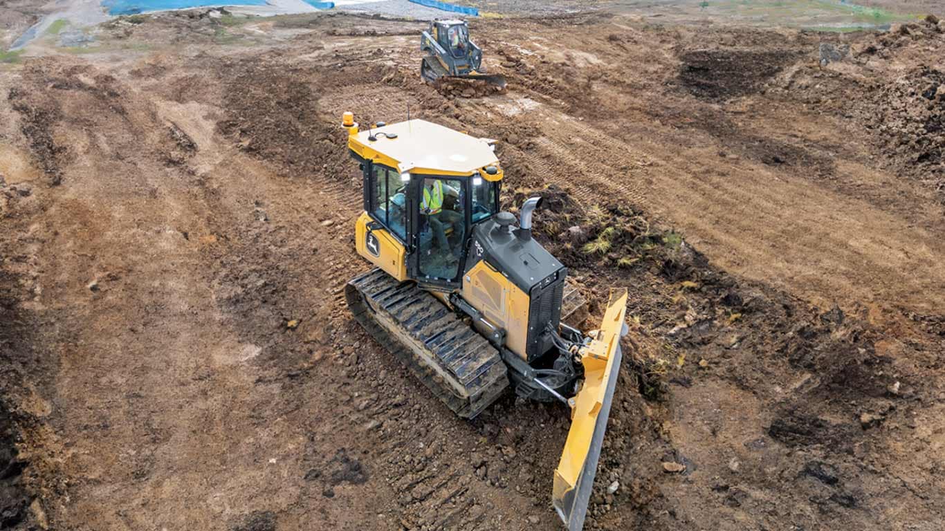 Deux bouteurs nivelant la terre sur un chantier de construction, un au premier plan avec l’utilisateur visible.