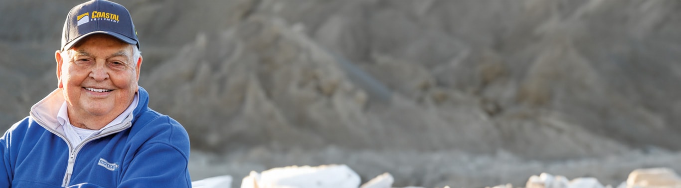Person in blue jacket and cap with 'Coastal Equipment' logo, standing in front of a rocky landscape.