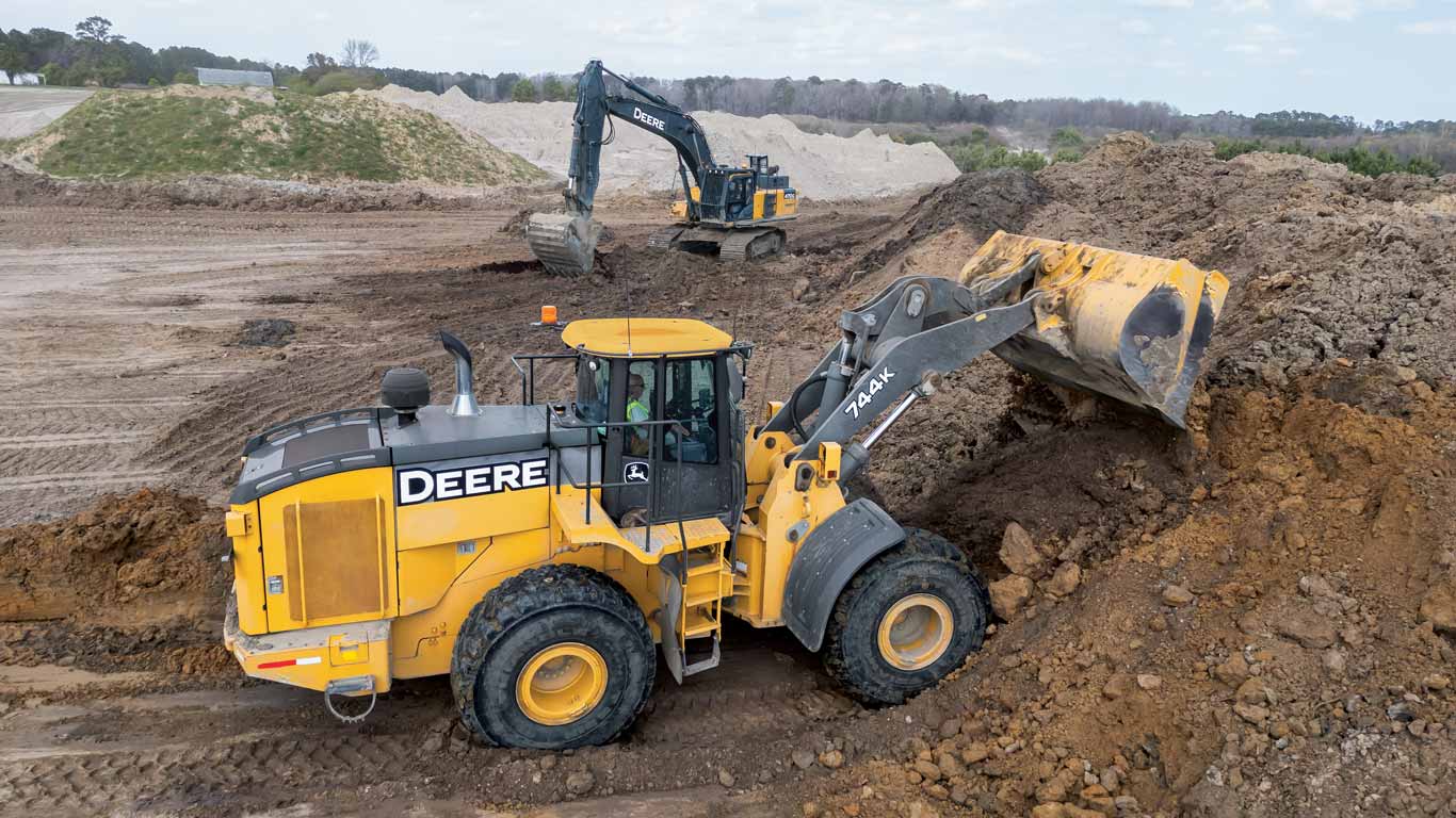 Deux véhicules de construction John Deere déplaçant de la terre sur un grand chantier ouvert.
