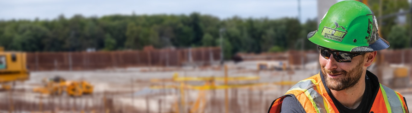 Travailleur avec un casque de protection vert et un gilet orange sur le chantier.