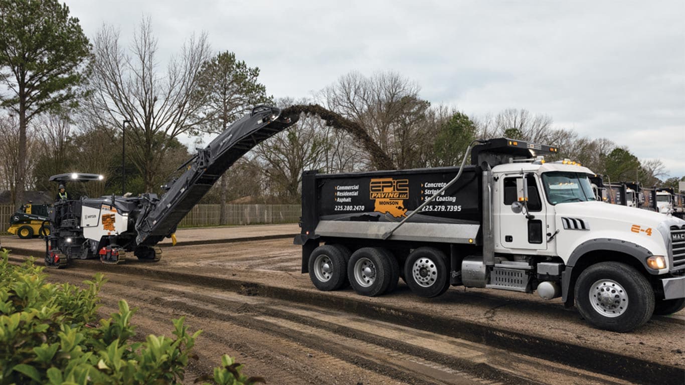A compact milling machine filling a dump truck on a work site