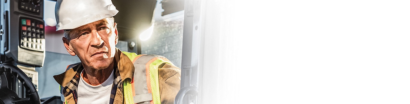 Bill Stanley peers out from the cab of a John Deere 772 P-Tier Motor Grader.