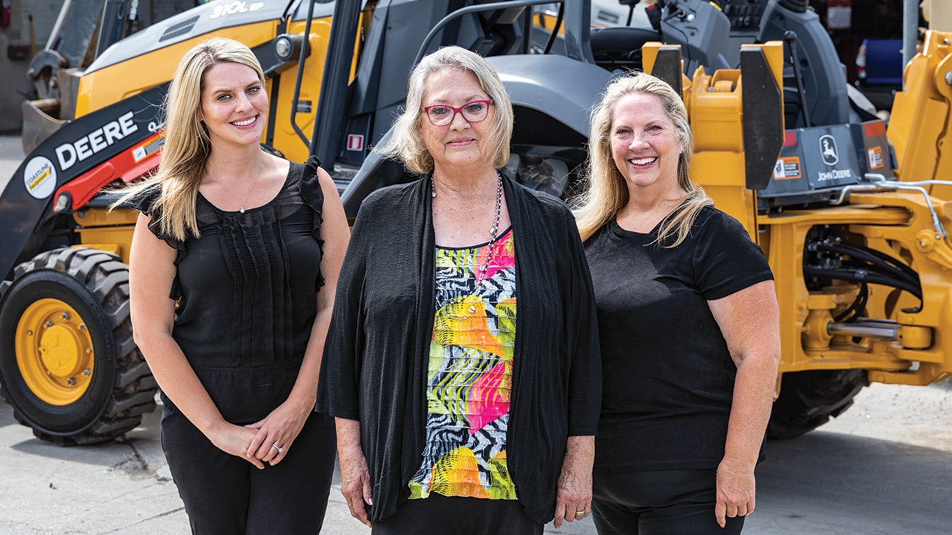 Représentant trois générations, Amanda Matson, Janet Ferguson et Nikki Worden de Newman Backhoe Service se tiennent devant une rétrocaveuse 310L de John Deere.