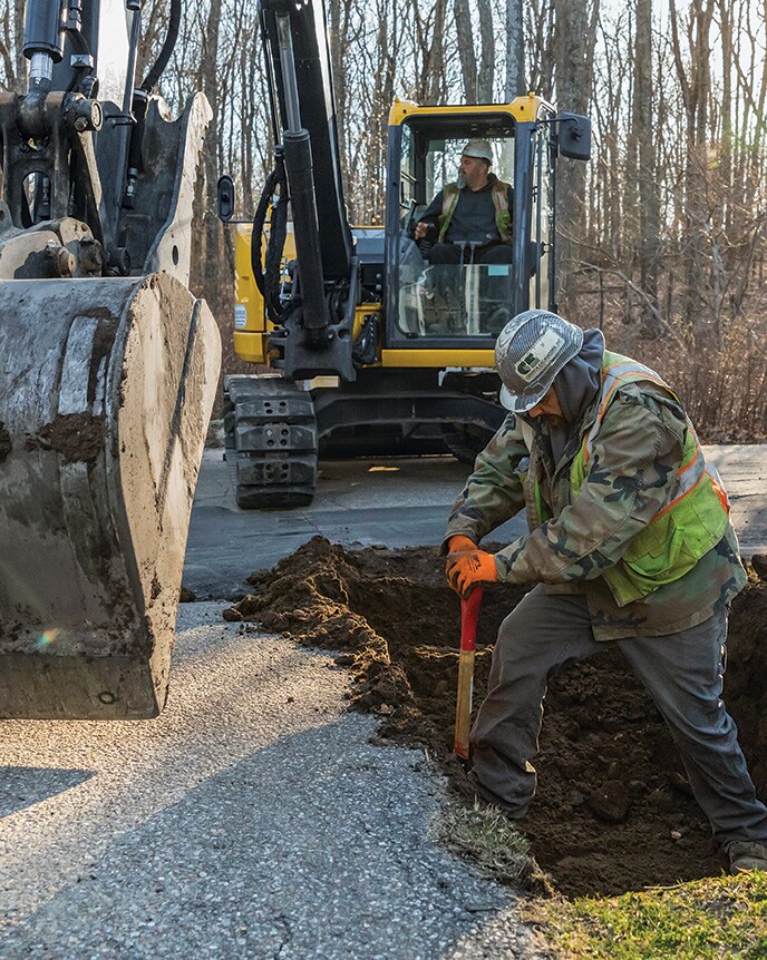 Michael Flaherty operates a John Deere 85G Excavator as Jacob Pepin prepares the hole for the shoring box.