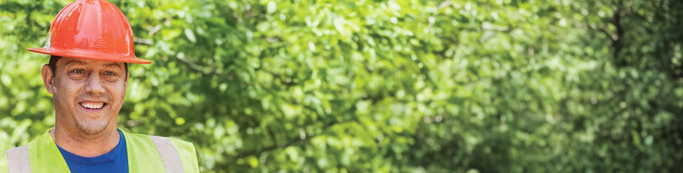 Travailleur de la construction portant un casque rouge, qui sourit, avec une forêt en arrière-plan