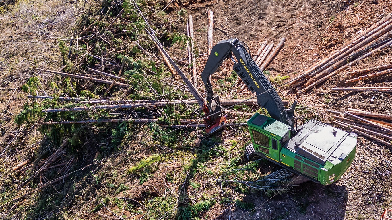 Vue aérienne d’une machine d’exploitation forestière avec un bras étendu, traitant du bois sur un site forestier entouré de tronçons d’arbre.