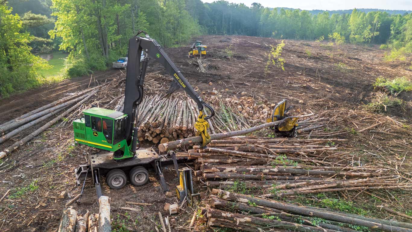 Logging machines stacking cut logs in a cleared forest area during timber operations.