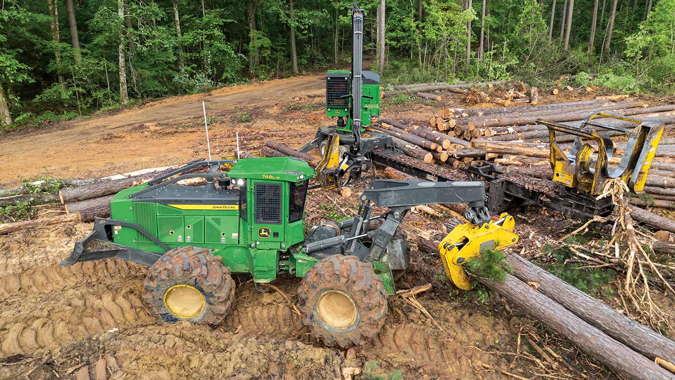 Two green forestry machines in forest; one lifts logs with a yellow grapple.
