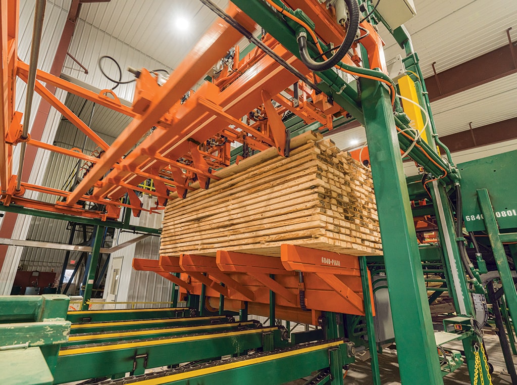 The stacker is lifting the finished pile of cut lumber with spacers to be strapped.