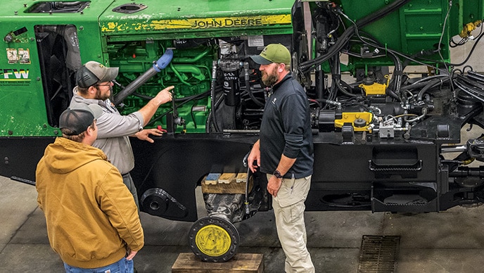 Three Foster F Wineland employees discuss the Powertrain ReLife Plus machine rebuild progress alongside a 743H Grapple Skidder.