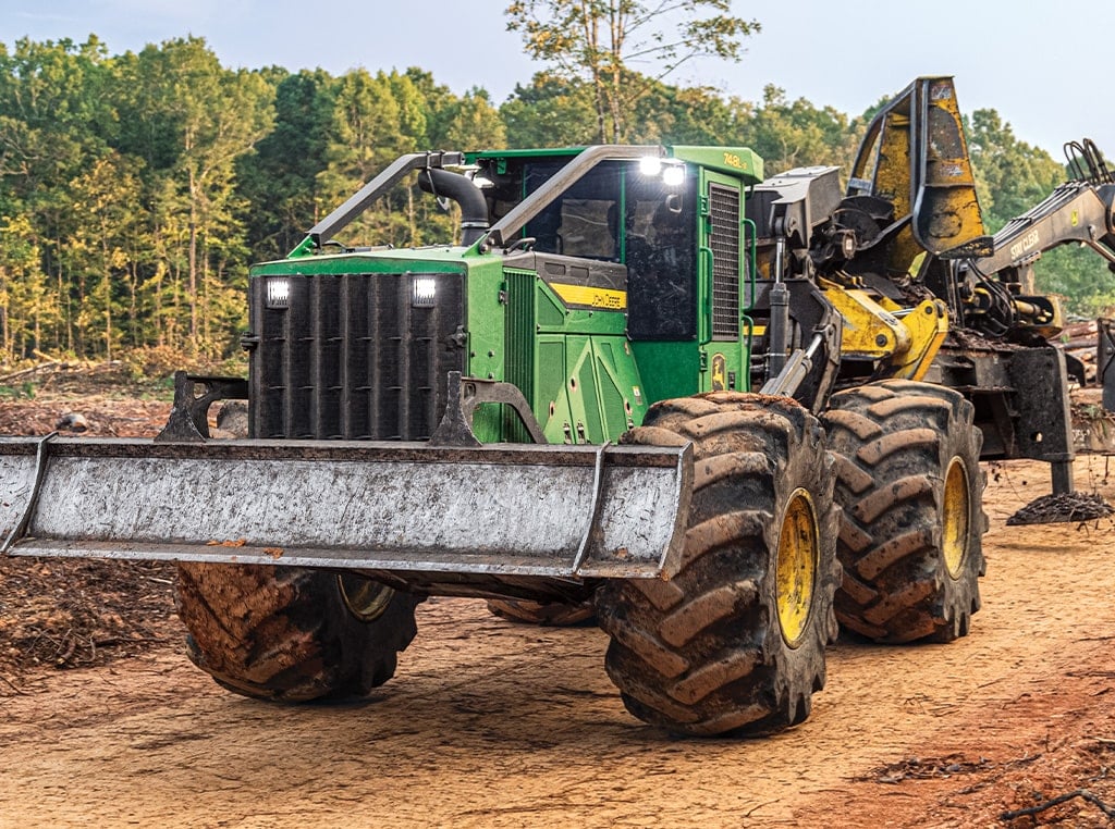 The 748L-II Grapple Skidder drives away from a 437E Knuckleboom Loader, sorts, and piles felled trees.