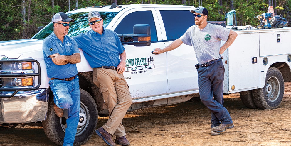 Randy Wilkes, Dobbs Equipment dealer representative, talks with father and son owners Bud West of Brown Chapel Logging and Matt West of West Forest Products.