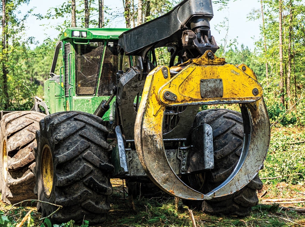 A 748L-II Grapple Skidder seen from the back drives into the woods.
