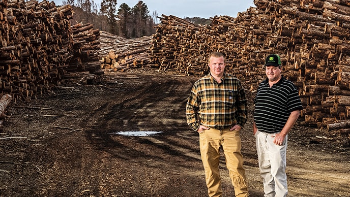 Ryan, le fils, pose à gauche de son père Edwin sur le chemin forestier, avec du bois dur empilé des deux côtés, dans le parc à bois chez Edwin Taylor & Son Logging à Duck Hill, dans le Mississippi.