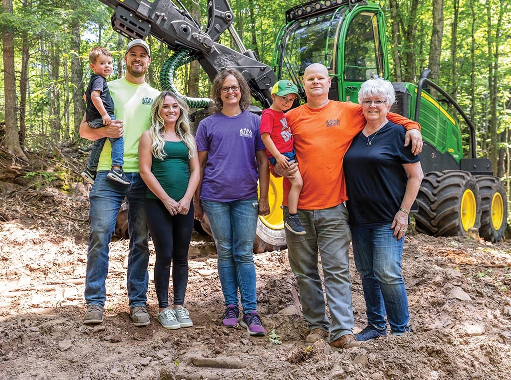 Plusieurs générations de la famille Harju se tiennent ensemble dans une forêt à côté d'une abatteuse-façonneuse à roues 1270G.