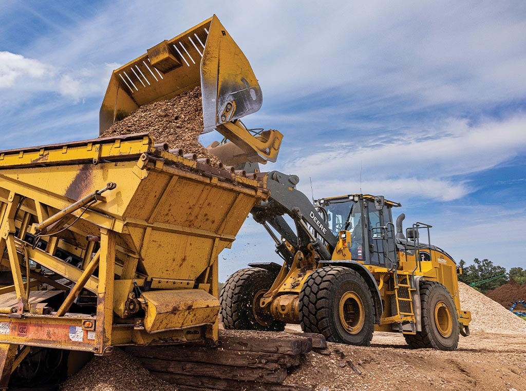 A 744L Wheel Loader dumps a full bucket of woodchips into a dump box that is attached to a conveyor.