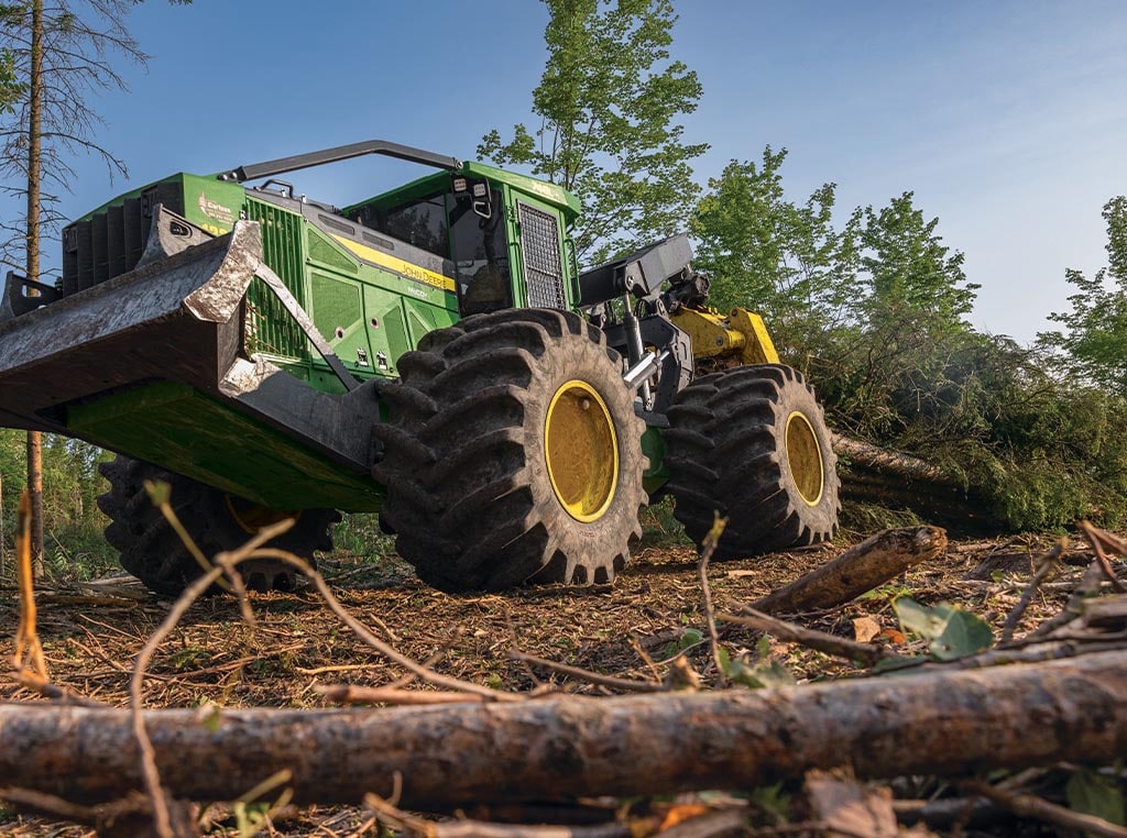 Une débardeuse 748L-II traîne des arbres entiers dans sa pince à travers une forêt.