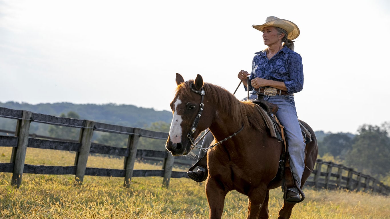 Woman horseback riding through field.