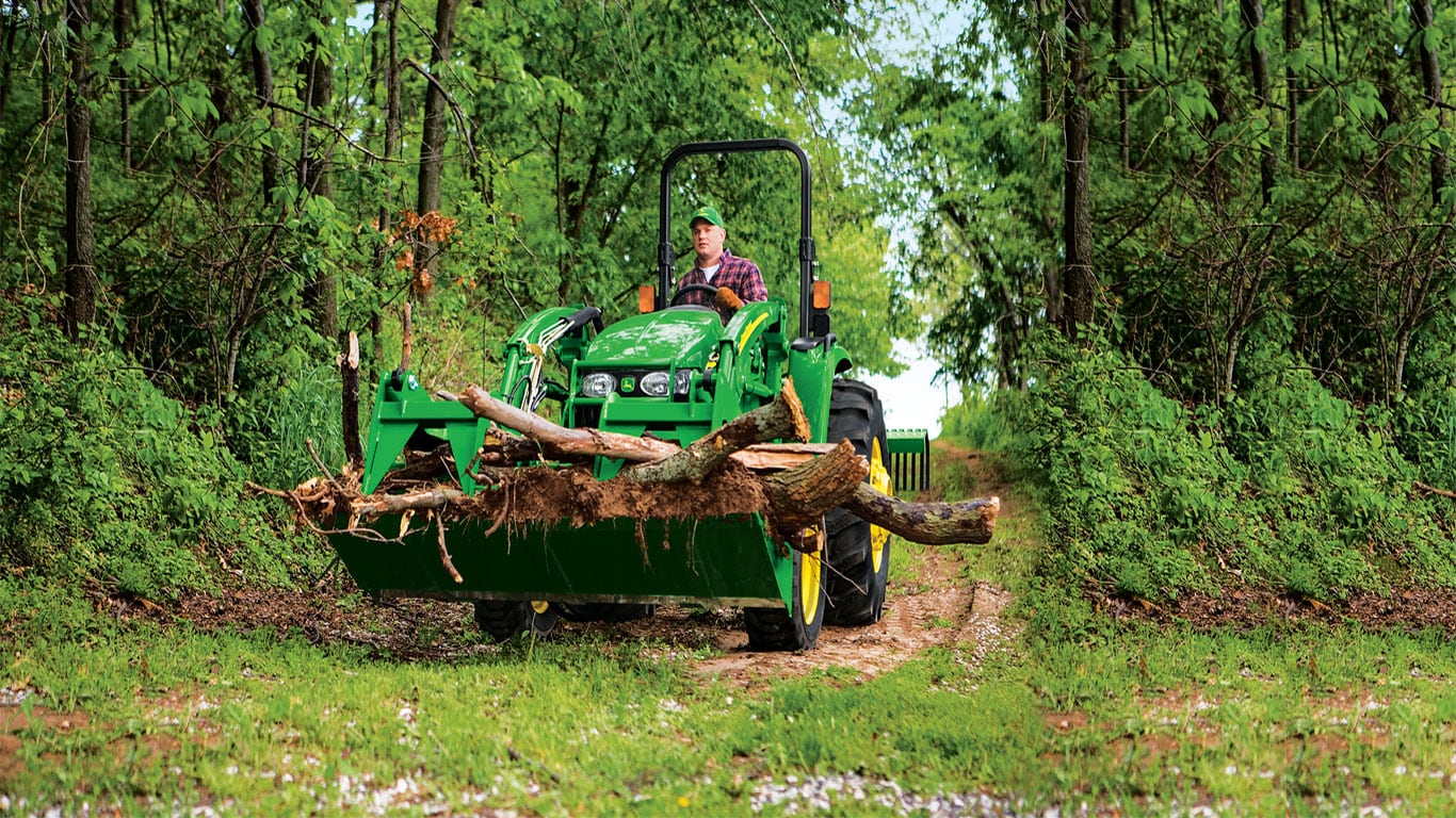 Homme dans les bois qui conduit un tracteur pour transporter des branches d’arbre