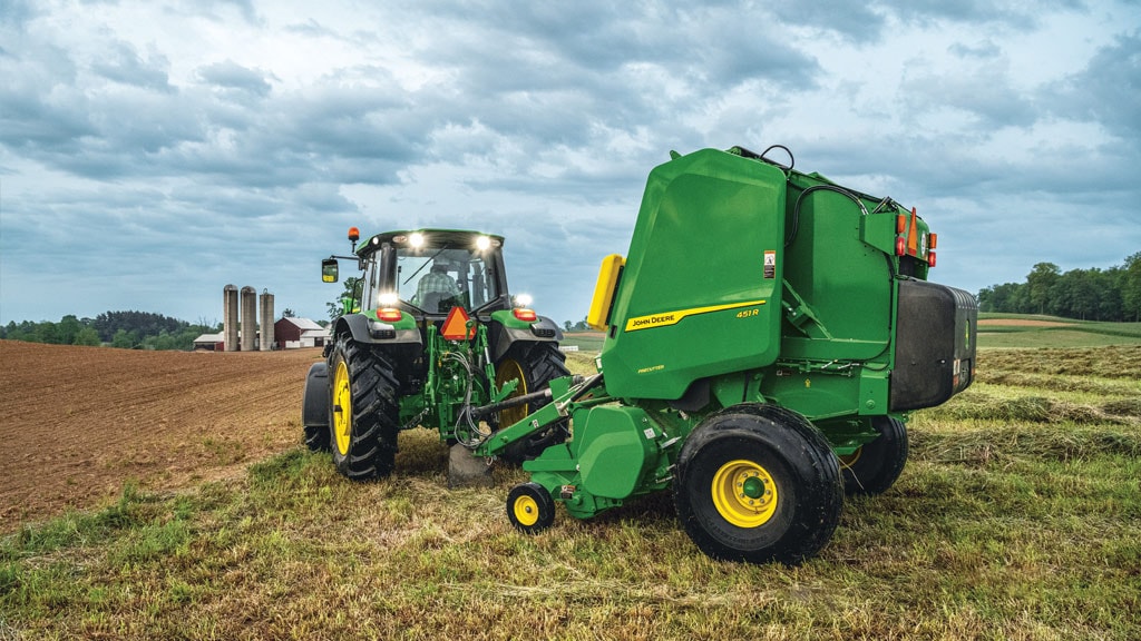 Tracteur, les phares allumés, en train de tirer une rotopresse 451R dans un champ