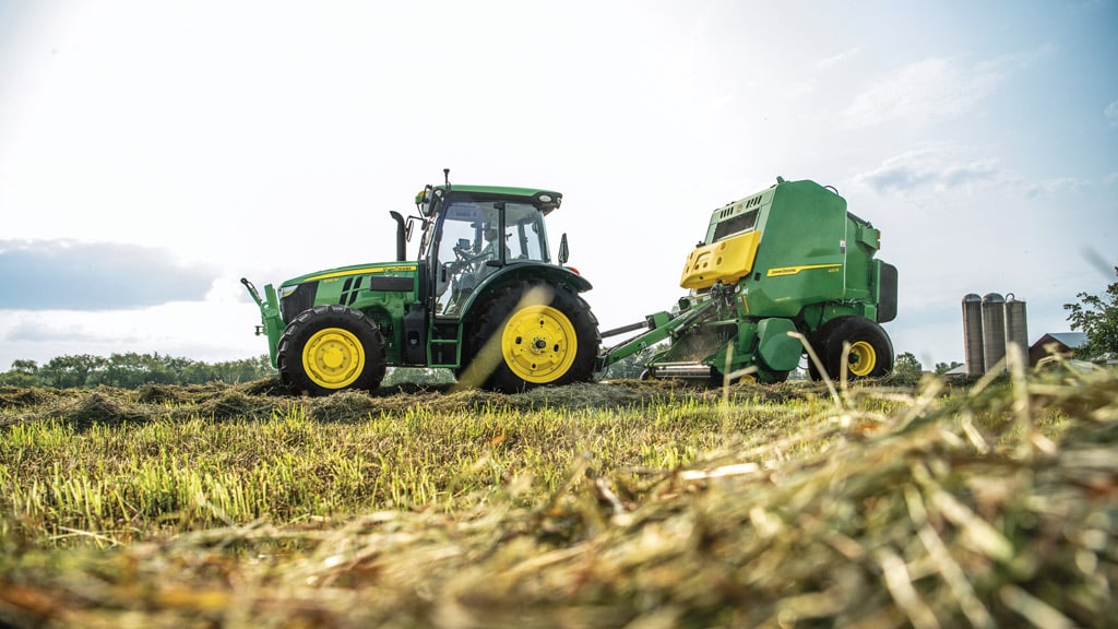 Tracteur 5130M tirant une presse 451R en train de mettre du foin en balles dans le champ d'une exploitation agricole