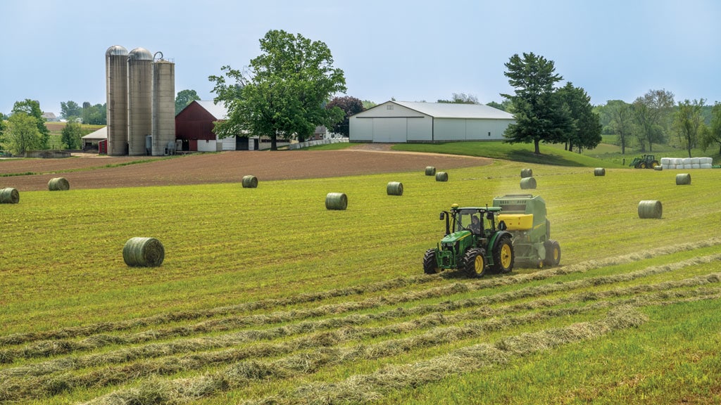 Tracteur 5130M tirant une rotopresse dans un champ et balles rondes éparpillées dans ce même champ