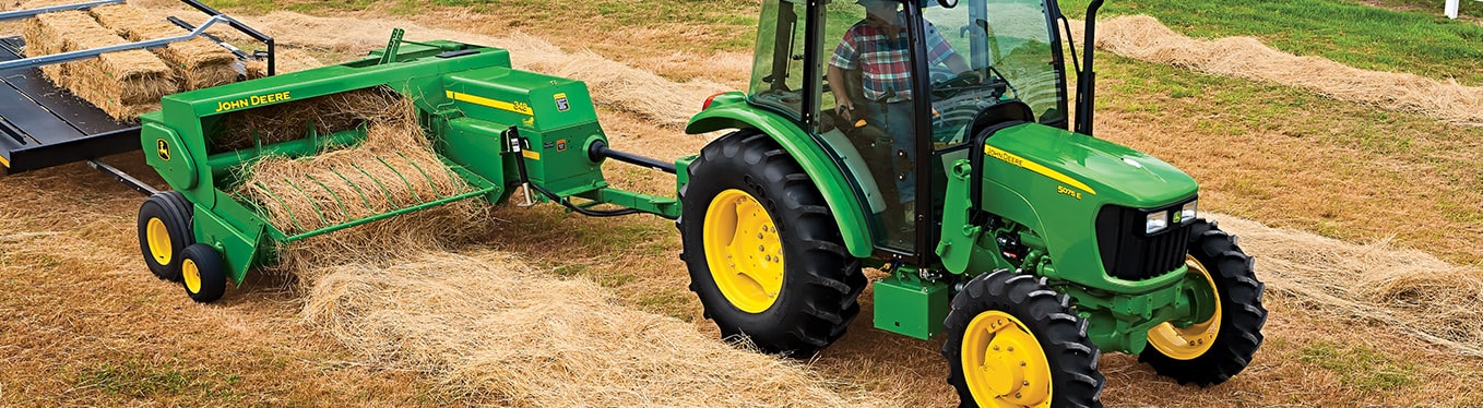 Tractor and small square baler working in field.